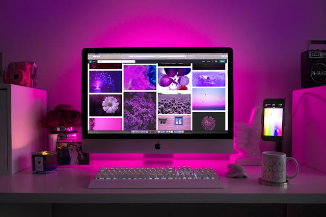 Desktop workspace with an iMac displaying a purple-toned image gallery under pink lighting