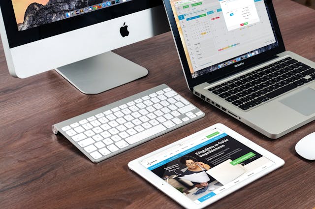 Desktop computer, laptop, keyboard, and tablet arranged on a wooden desk
